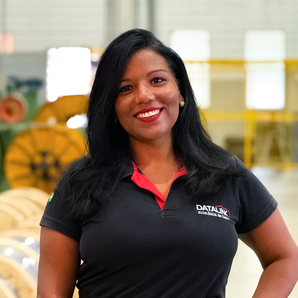 Esta imagem mostra nossa vendendora Fabiana Brito vestindo uma camisa polo preta e vermelha com o logotipo “Datalink, Tecnologia em cabos”, em um fundo branco.