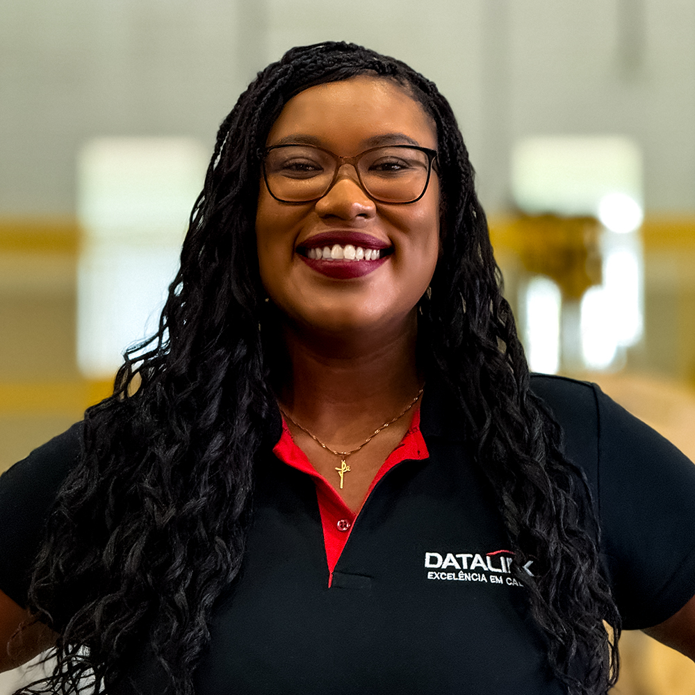 Esta imagem mostra nossa vendendora Jaíne Ferreira vestindo uma camisa polo preta e vermelha com o logotipo “Datalink, Tecnologia em cabos”, em um fundo branco.